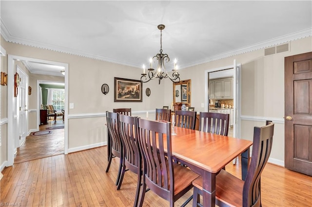 dining space featuring light hardwood / wood-style floors, crown molding, and an inviting chandelier