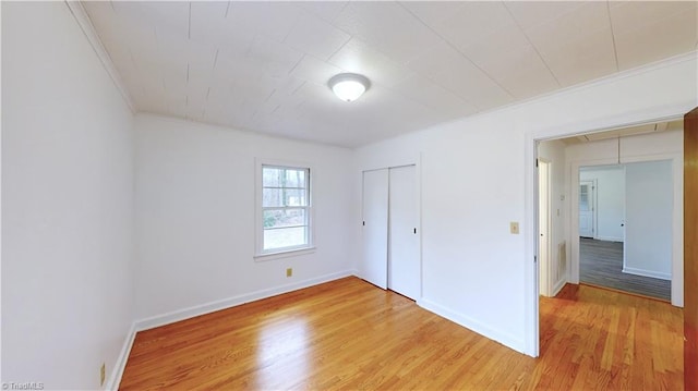 unfurnished bedroom with a closet, ornamental molding, and light wood-type flooring