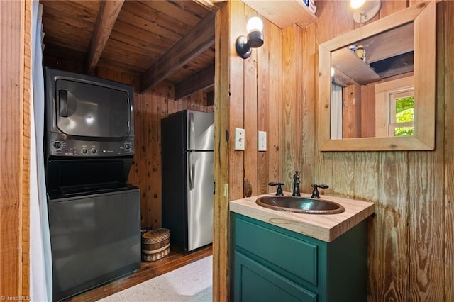 bathroom featuring vanity, stacked washer and dryer, beam ceiling, wooden walls, and wooden ceiling
