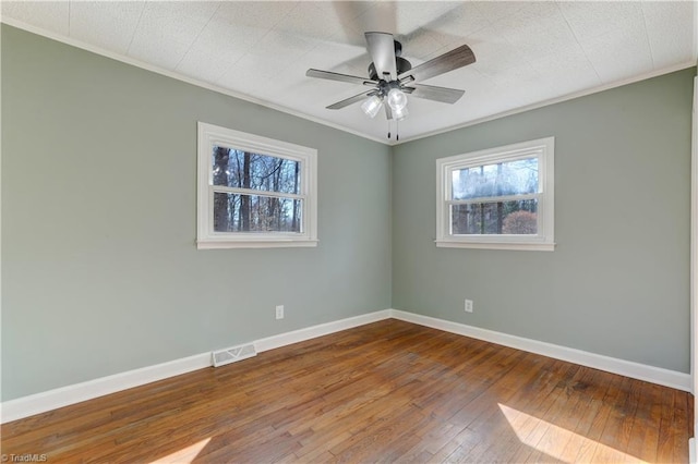 empty room featuring wood-type flooring, visible vents, ornamental molding, a ceiling fan, and baseboards