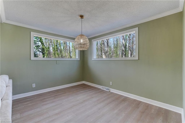 empty room with crown molding, visible vents, a textured ceiling, wood finished floors, and baseboards