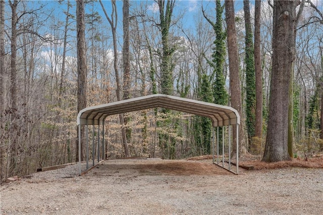 view of community with driveway, a detached carport, and a view of trees