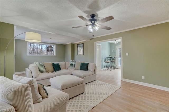 living room with a textured ceiling, ornamental molding, light wood-style flooring, and baseboards