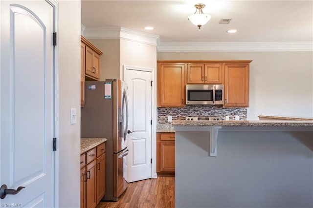 kitchen featuring a kitchen breakfast bar, stainless steel appliances, ornamental molding, and hardwood / wood-style flooring