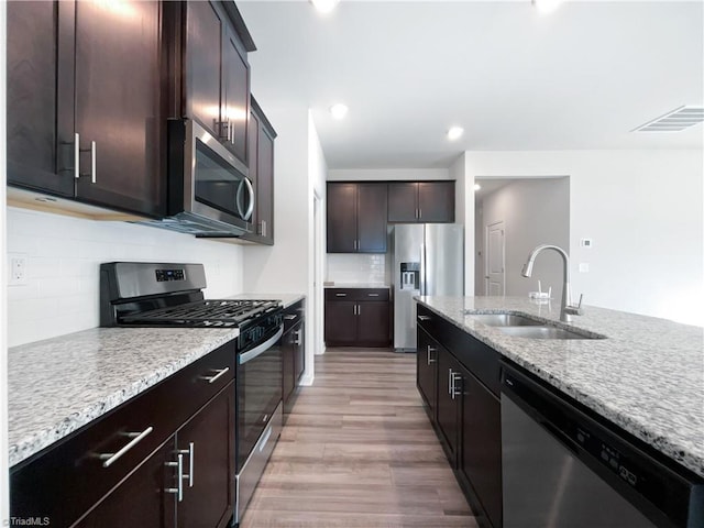 kitchen with sink, light hardwood / wood-style flooring, appliances with stainless steel finishes, dark brown cabinetry, and light stone countertops