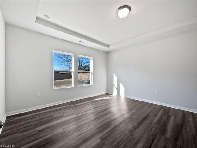 spare room with a tray ceiling and dark wood-type flooring