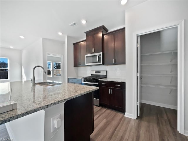 kitchen with sink, appliances with stainless steel finishes, dark hardwood / wood-style floors, dark brown cabinetry, and light stone countertops