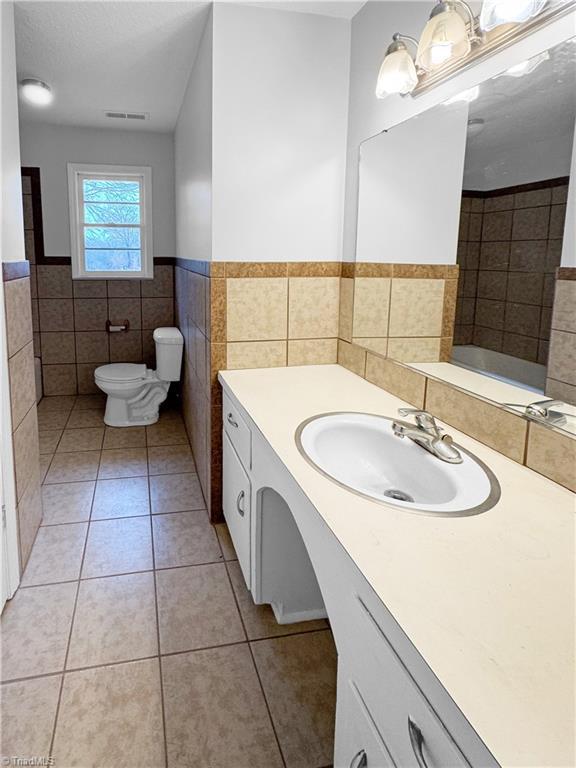 bathroom with tile patterned flooring, vanity, toilet, and tile walls