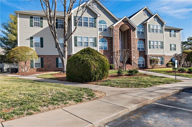 view of property featuring brick siding, central AC unit, and a front yard