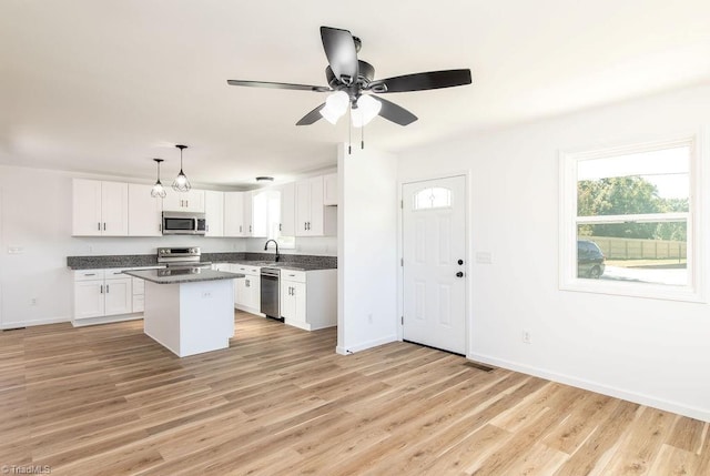 kitchen with white cabinets, a kitchen island, light wood-type flooring, pendant lighting, and stainless steel appliances