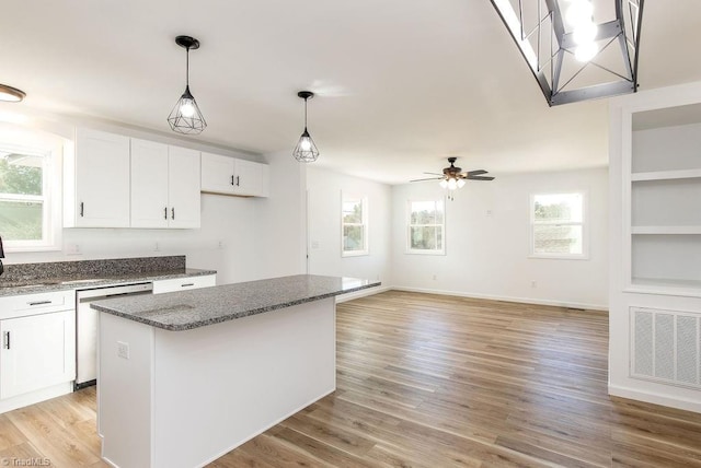 kitchen featuring a center island, light hardwood / wood-style floors, stainless steel dishwasher, white cabinets, and dark stone countertops