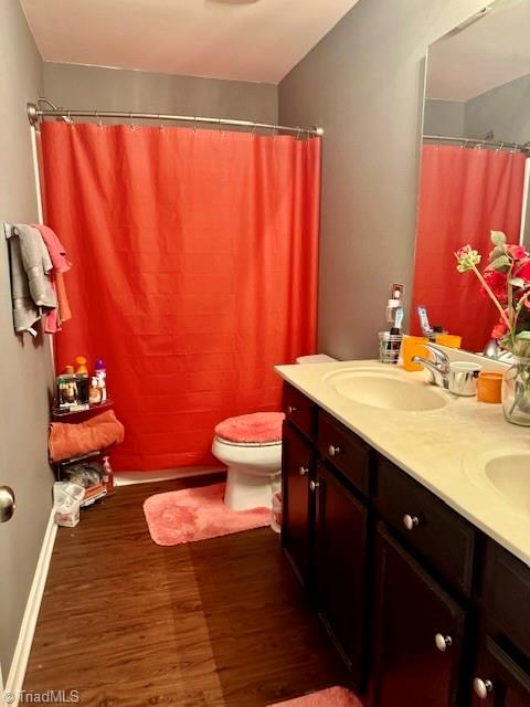 full bath with toilet, wood finished floors, a sink, baseboards, and double vanity