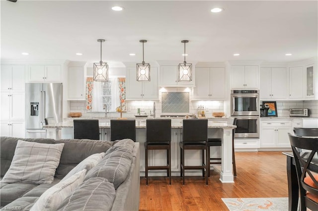 kitchen featuring white cabinets, a breakfast bar, open floor plan, stainless steel appliances, and light wood-style floors