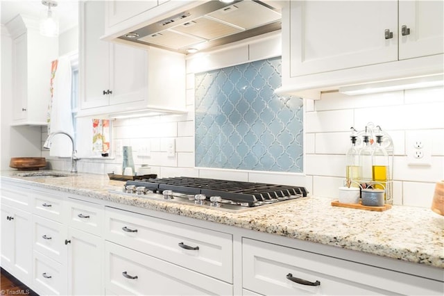 kitchen featuring premium range hood, stainless steel gas cooktop, white cabinets, and backsplash