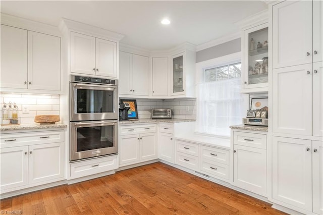 kitchen with light wood finished floors, stainless steel double oven, backsplash, and white cabinetry