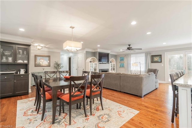 dining space featuring light wood-style flooring, recessed lighting, a fireplace, a ceiling fan, and ornamental molding