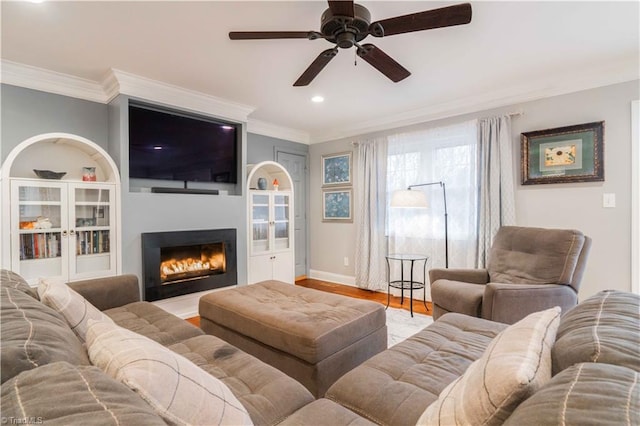 living room featuring baseboards, a lit fireplace, ornamental molding, and wood finished floors