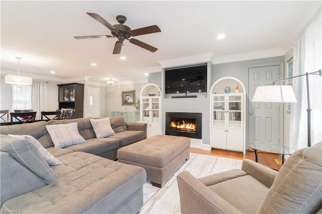 living room featuring a lit fireplace, ornamental molding, light wood-type flooring, and recessed lighting