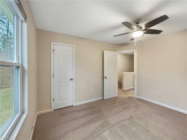 unfurnished bedroom featuring multiple windows, light colored carpet, and ceiling fan