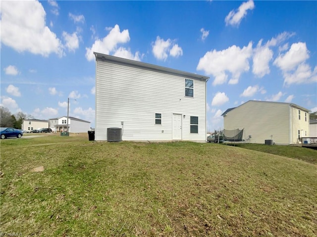 rear view of property with a trampoline, central AC unit, and a lawn