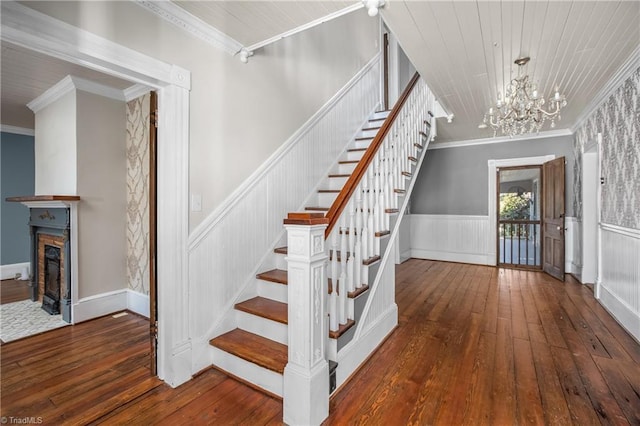 stairway featuring hardwood / wood-style flooring, ornamental molding, wainscoting, and a chandelier