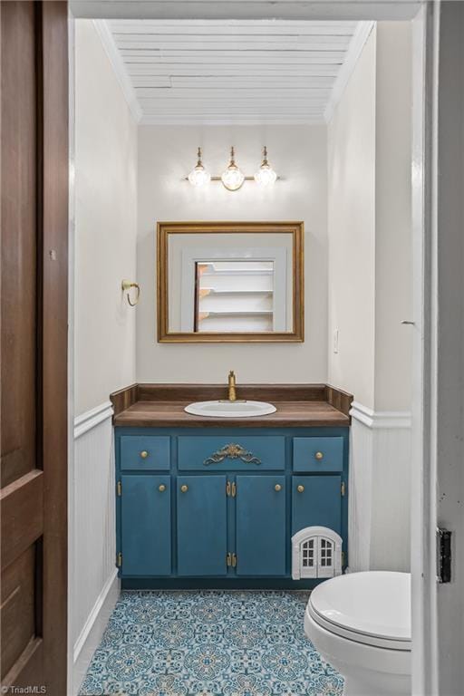 half bathroom featuring a wainscoted wall, vanity, and crown molding