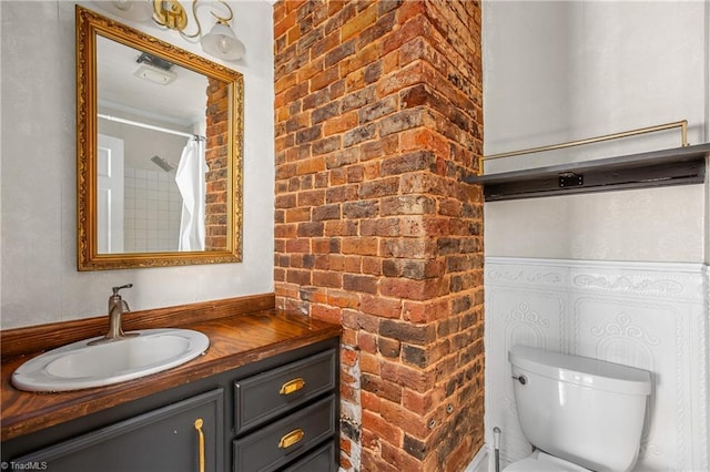 bathroom featuring toilet, brick wall, and vanity