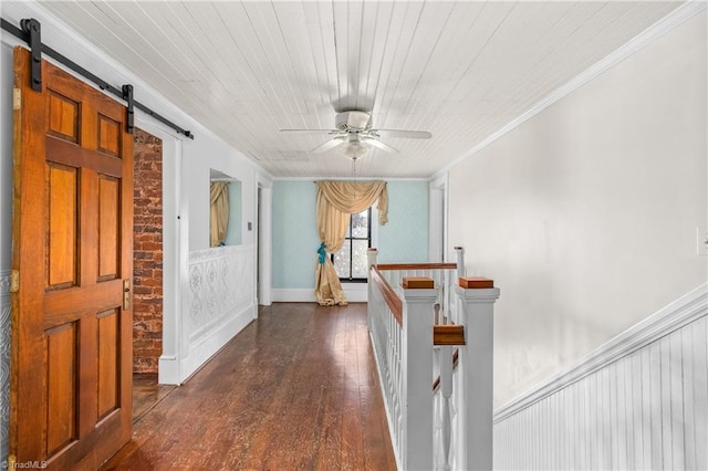 hall with ornamental molding, dark wood-type flooring, wainscoting, a barn door, and an upstairs landing