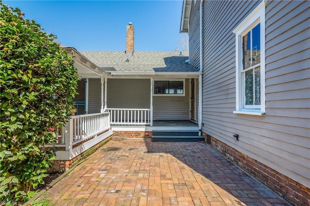 property entrance with covered porch and a shingled roof