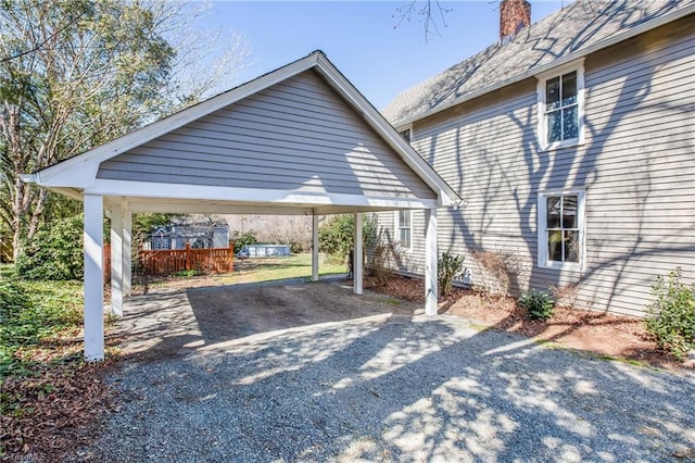 view of car parking featuring gravel driveway, a detached carport, and fence