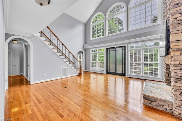 608 Greyrock Rd, Whitsett, NC 27377 - unfurnished living room featuring high vaulted ceiling, wood finished floors, stairway, arched walkways, and baseboards