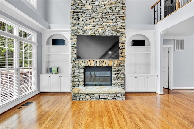 608 Greyrock Rd, Whitsett, NC 27377 - unfurnished living room featuring built in shelves, wood finished floors, baseboards, a stone fireplace, and a high ceiling