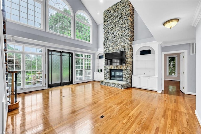 608 Greyrock Rd, Whitsett, NC 27377 - unfurnished living room featuring light wood-type flooring, high vaulted ceiling, a stone fireplace, ornamental molding, and built in shelves