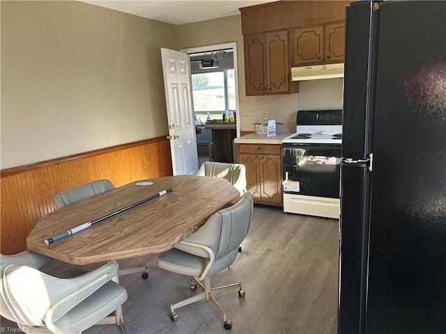 kitchen with wooden walls, white electric range, wood-type flooring, and black fridge