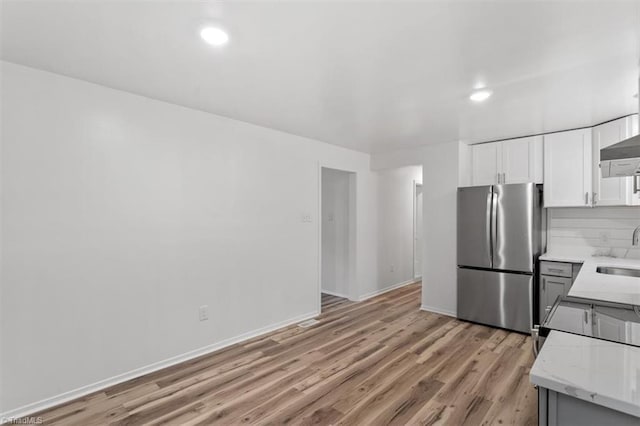 kitchen with sink, white cabinetry, stainless steel refrigerator, light stone countertops, and light hardwood / wood-style floors