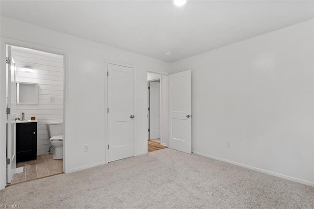 unfurnished bedroom with ensuite bathroom and light colored carpet