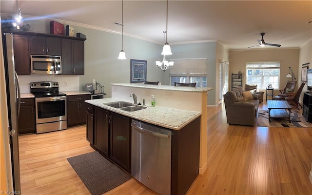 kitchen with stainless steel appliances, light wood-style floors, ornamental molding, open floor plan, and a sink