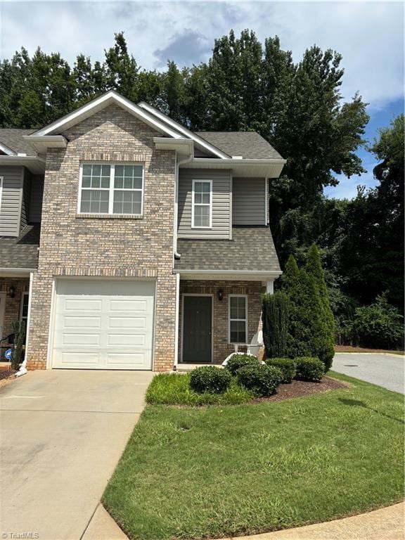 view of front of home featuring an attached garage, brick siding, concrete driveway, roof with shingles, and a front yard