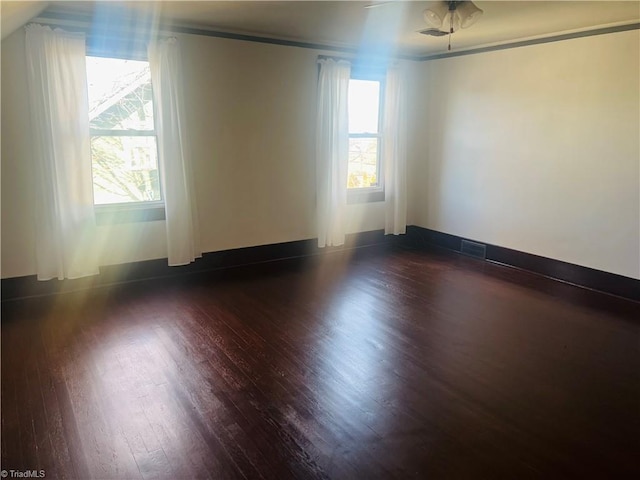 empty room with dark wood-type flooring, a wealth of natural light, and ceiling fan