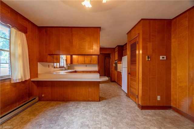 kitchen with kitchen peninsula, wall oven, baseboard heating, wooden walls, and white refrigerator