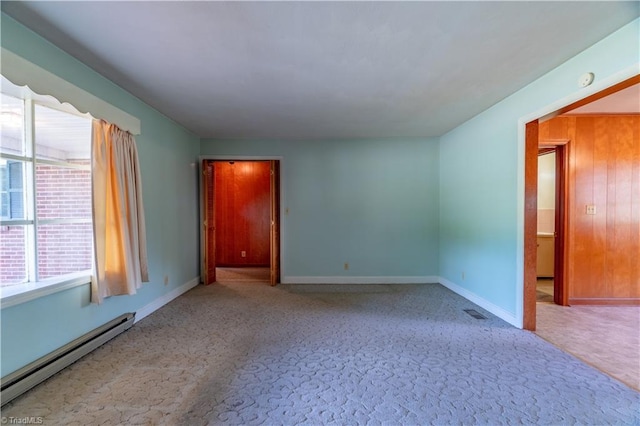 spare room featuring light colored carpet, a baseboard heating unit, and wood walls