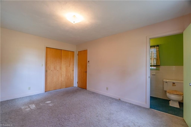 unfurnished bedroom featuring carpet floors, ensuite bathroom, a closet, and tile walls