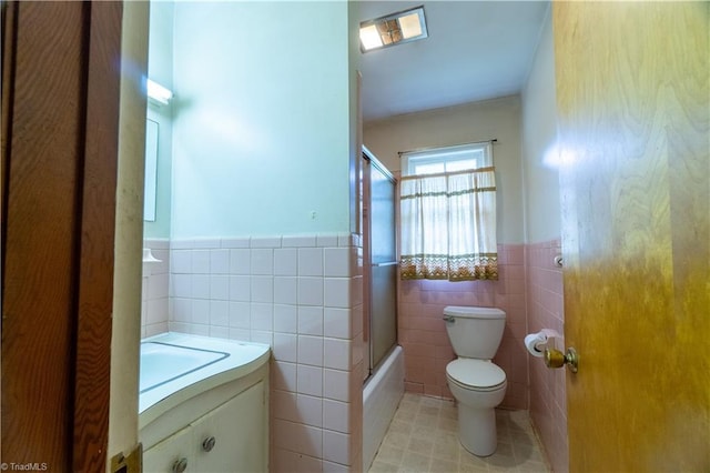 full bathroom with tile patterned flooring, bath / shower combo with glass door, toilet, vanity, and tile walls