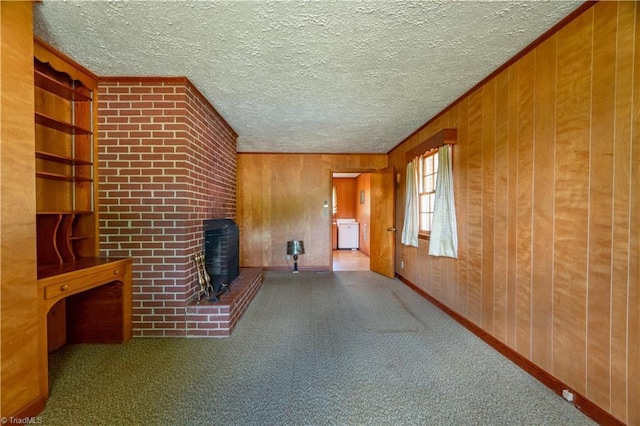 unfurnished living room with a brick fireplace, wood walls, crown molding, carpet floors, and a textured ceiling