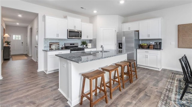 kitchen with white cabinetry, stainless steel appliances, and a center island with sink