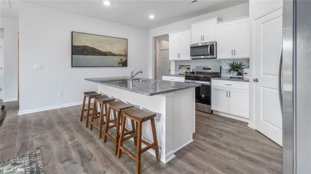 kitchen featuring sink, a kitchen island with sink, stainless steel appliances, white cabinets, and dark stone counters