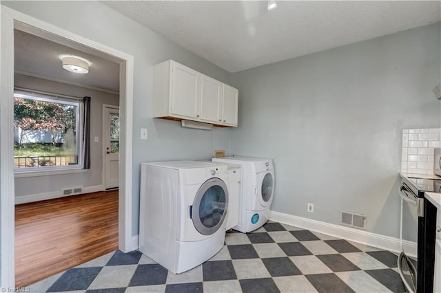 clothes washing area featuring a textured ceiling, cabinets, and separate washer and dryer