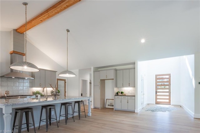 kitchen featuring decorative backsplash, a kitchen breakfast bar, light stone counters, beamed ceiling, and light hardwood / wood-style floors