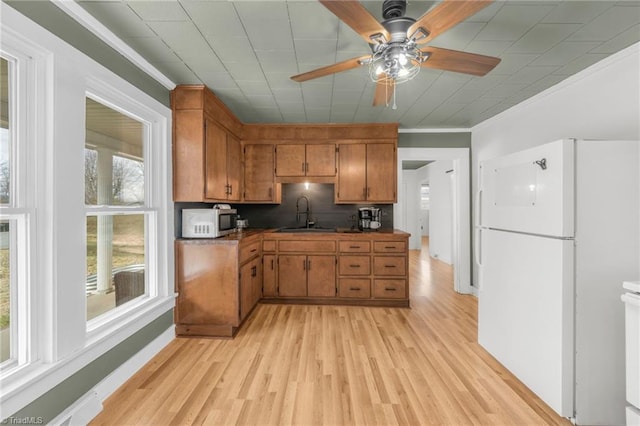 kitchen featuring stainless steel microwave, ornamental molding, freestanding refrigerator, brown cabinetry, and dark countertops