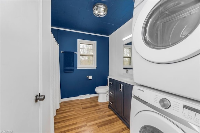 full bath featuring stacked washer and dryer, baseboards, toilet, wood finished floors, and vanity